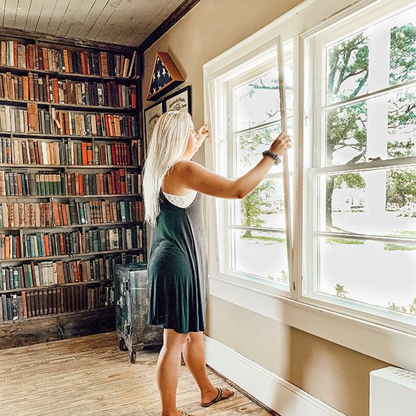 woman installing Indow window inserts to reduce noise next to bookshelves